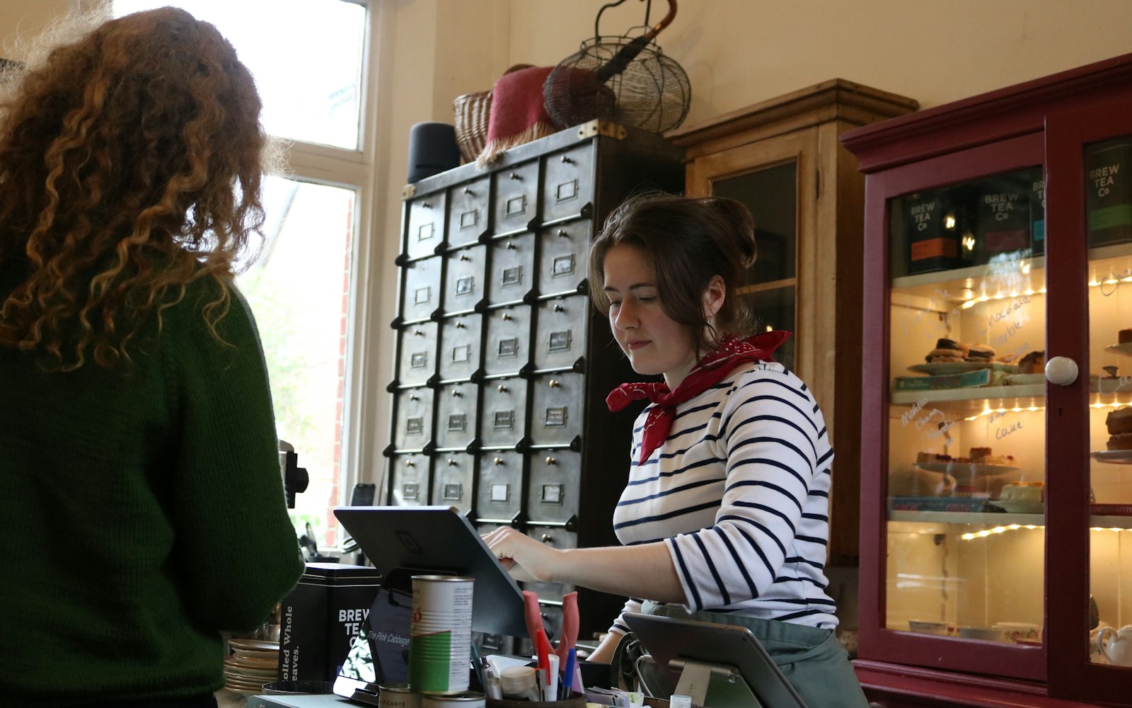 A cashier helping a customer at a cafe counter with a tablet point-of-sale system